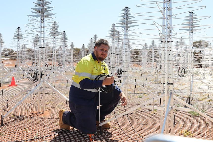 A man is kneeling on the ground next to the antenna of the Christmas tree.